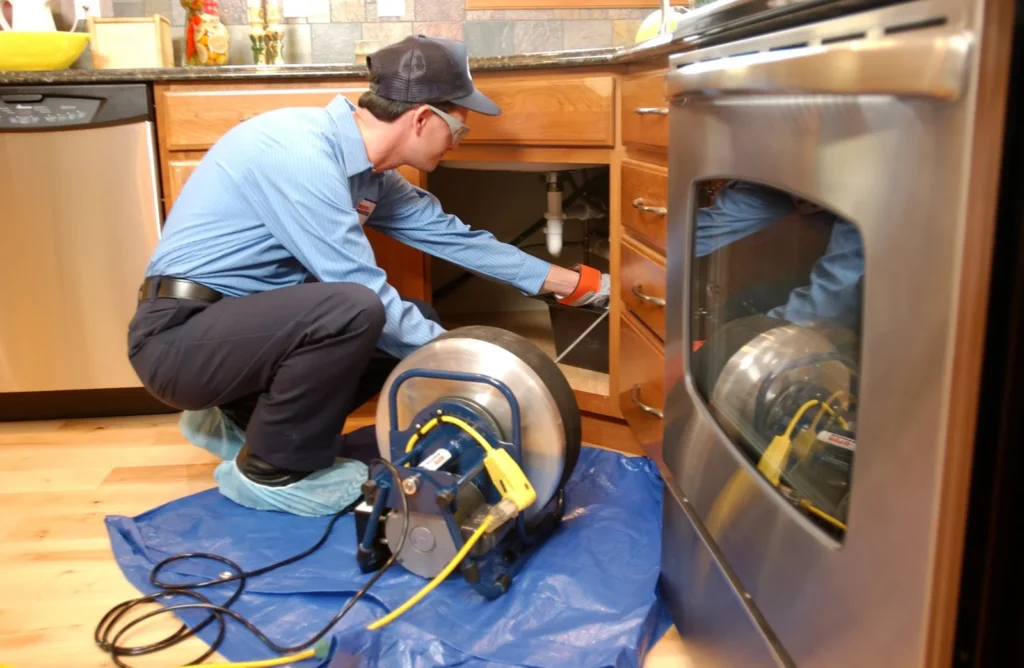 Professional plumber using advanced machinery for drain cleaning services in a residential kitchen
